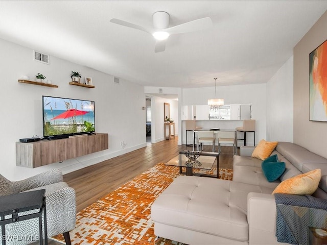 living room featuring ceiling fan with notable chandelier and light hardwood / wood-style floors