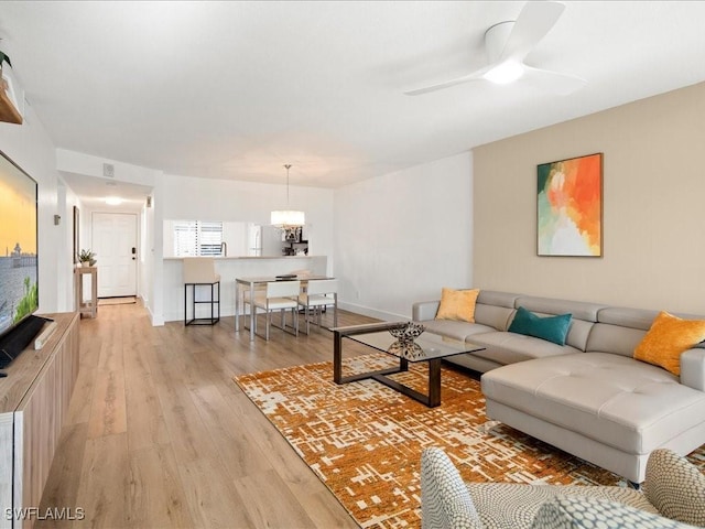 living room with ceiling fan with notable chandelier and light hardwood / wood-style floors