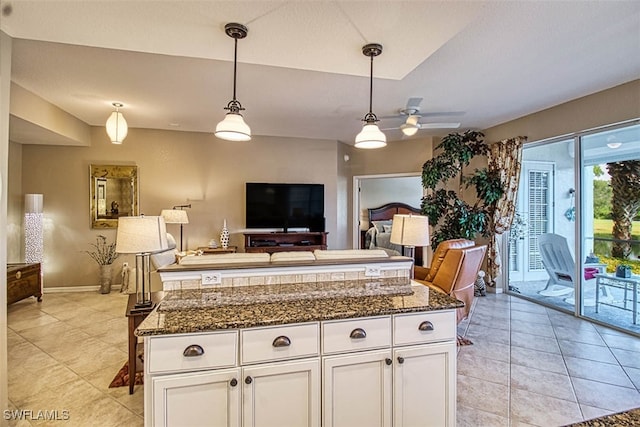 kitchen with a kitchen island, white cabinetry, ceiling fan, pendant lighting, and dark stone countertops