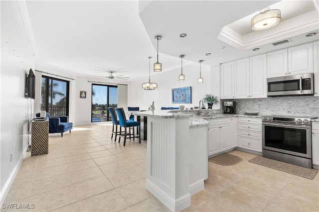 kitchen with white cabinets, appliances with stainless steel finishes, kitchen peninsula, and ornamental molding