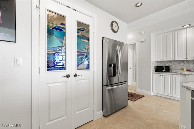 kitchen featuring white cabinets, stainless steel fridge, light stone countertops, light tile patterned floors, and tasteful backsplash