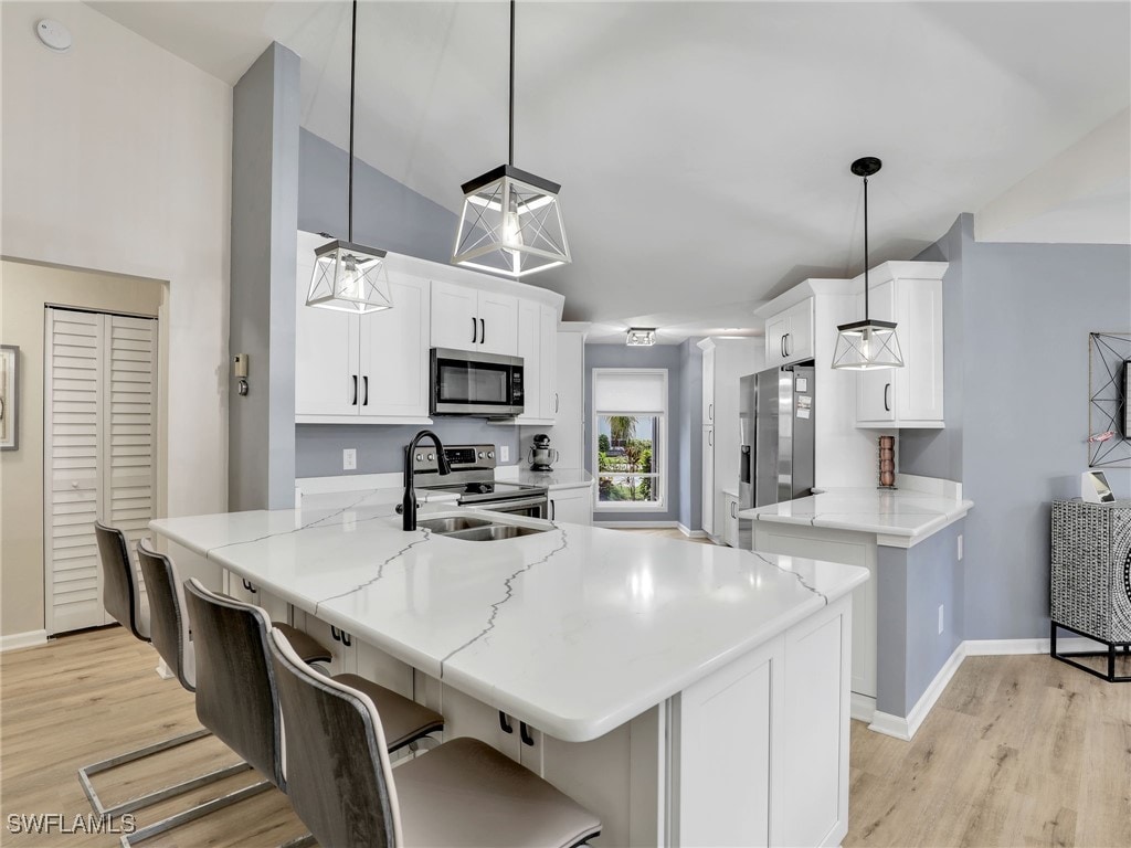 kitchen featuring light hardwood / wood-style floors, white cabinets, stainless steel appliances, and pendant lighting