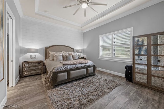 bedroom featuring hardwood / wood-style floors, ceiling fan, ornamental molding, and a tray ceiling