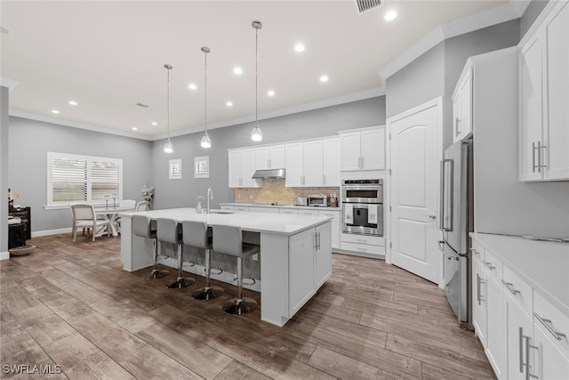 kitchen with hanging light fixtures, wood-type flooring, a kitchen island with sink, and stainless steel appliances