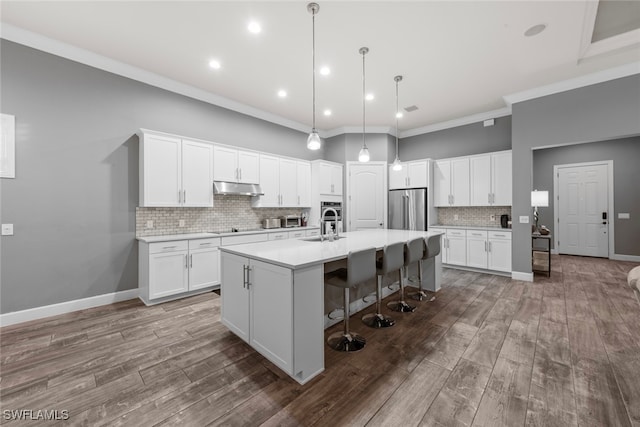 kitchen featuring a center island with sink, white cabinetry, ornamental molding, hanging light fixtures, and stainless steel fridge