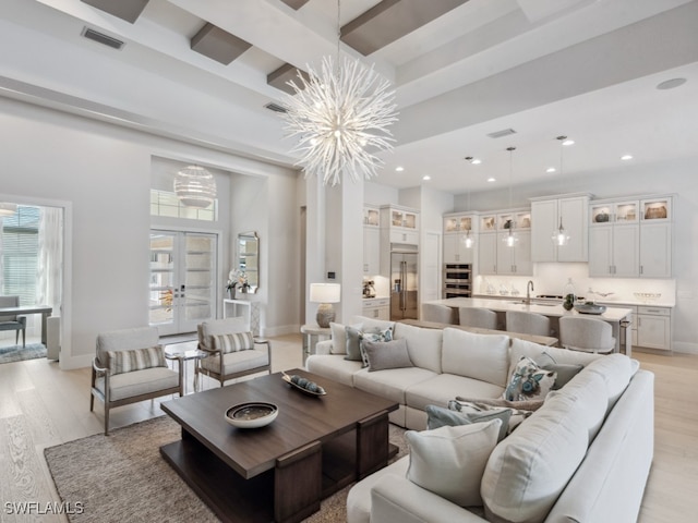 living room with sink, light wood-type flooring, french doors, beamed ceiling, and a notable chandelier