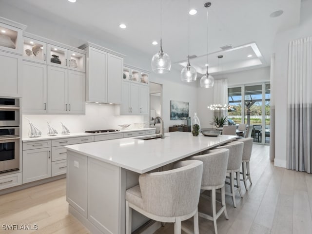 kitchen featuring white cabinetry, sink, pendant lighting, and an island with sink