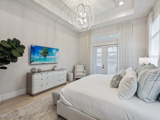 bedroom featuring a chandelier, a tray ceiling, multiple windows, and light wood-type flooring