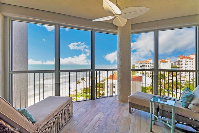 sunroom / solarium with a wealth of natural light, a water view, a view of the beach, and ceiling fan