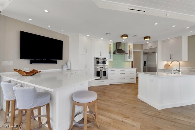 kitchen featuring white cabinets, sink, light hardwood / wood-style floors, wall chimney exhaust hood, and stainless steel appliances