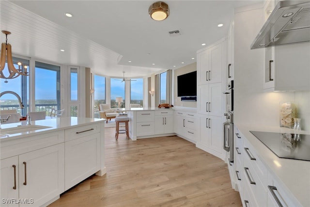 kitchen featuring sink, wall chimney range hood, a wealth of natural light, and white cabinets