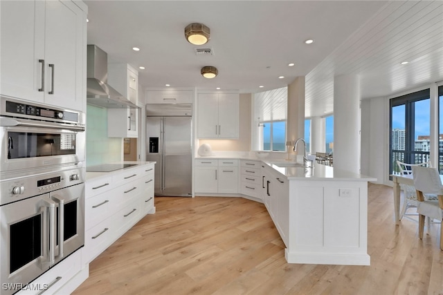 kitchen featuring wall chimney exhaust hood, white cabinets, stainless steel appliances, and light wood-type flooring