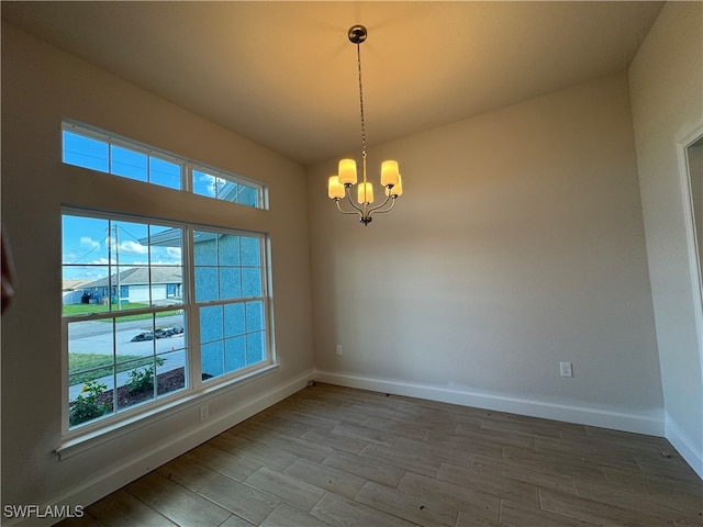 empty room with wood-type flooring and a notable chandelier