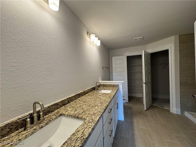 2112 NW 22nd Ave, Cape Coral, FL 33993 - full bathroom with a textured wall, a textured ceiling, double vanity, wood finished floors, and a tile shower