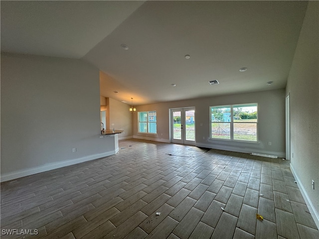 unfurnished living room with a chandelier, hardwood / wood-style floors, a healthy amount of sunlight, and lofted ceiling