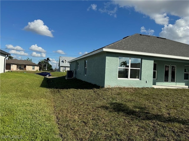 2112 NW 22nd Ave, Cape Coral, FL 33993 - rear view of property featuring stucco siding, a yard, roof with shingles, and central air condition unit
