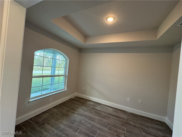 unfurnished room with a textured ceiling, a raised ceiling, and dark wood-type flooring