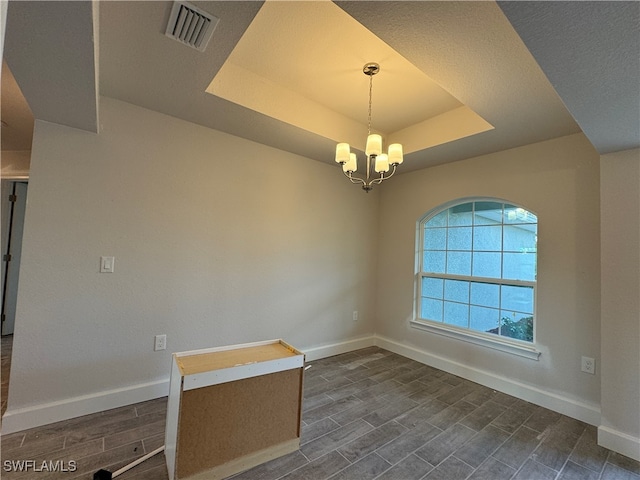 empty room featuring a chandelier, dark hardwood / wood-style floors, and a tray ceiling