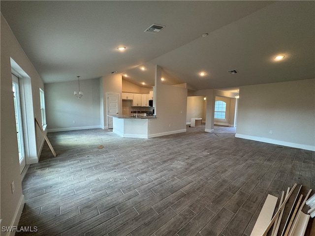 unfurnished living room with sink, hardwood / wood-style floors, vaulted ceiling, and a notable chandelier