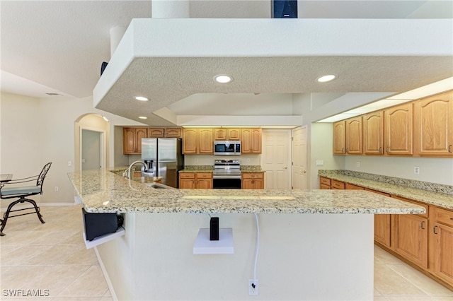 kitchen with a large island with sink, stainless steel appliances, and light tile patterned flooring