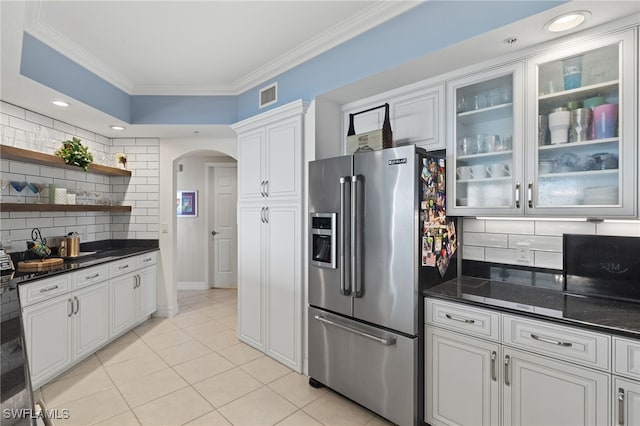 kitchen featuring high end fridge, backsplash, dark stone counters, ornamental molding, and white cabinetry