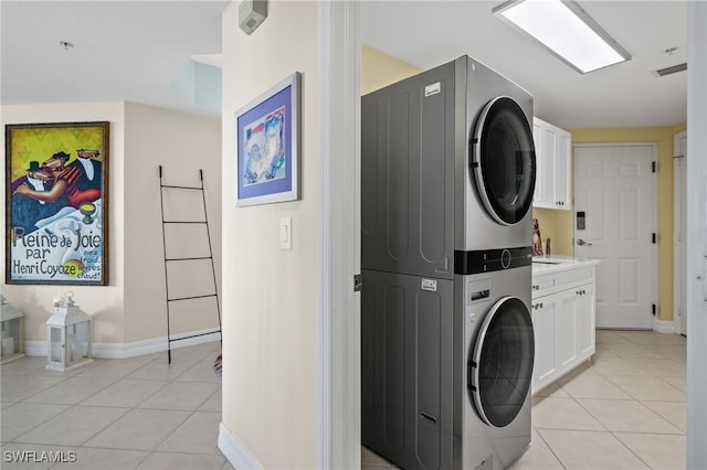 laundry room with stacked washer / drying machine, light tile patterned floors, and cabinets