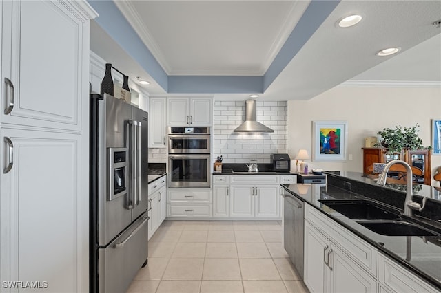 kitchen featuring wall chimney range hood, sink, white cabinets, appliances with stainless steel finishes, and tasteful backsplash