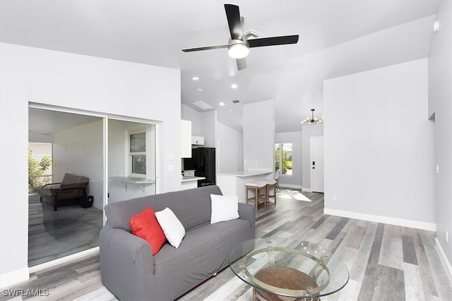 living room with light hardwood / wood-style flooring, ceiling fan with notable chandelier, and vaulted ceiling