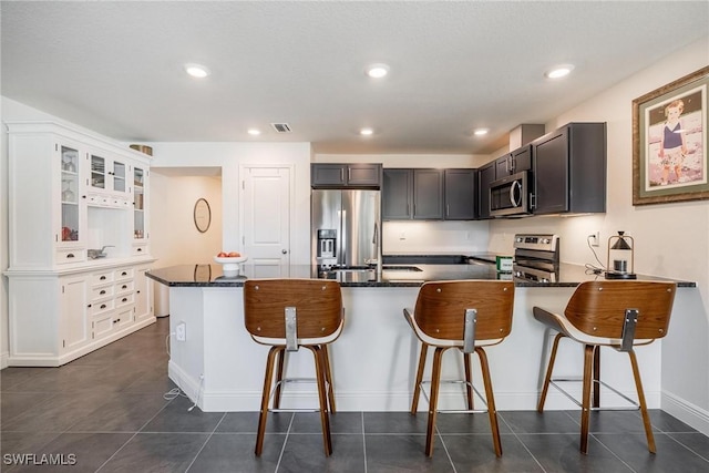 15050 Caspian Tern Ct Unit 102, North Fort Myers, FL 33917 - kitchen featuring a peninsula, dark stone counters, visible vents, glass insert cabinets, and appliances with stainless steel finishes