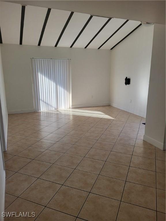 tiled empty room featuring vaulted ceiling with beams