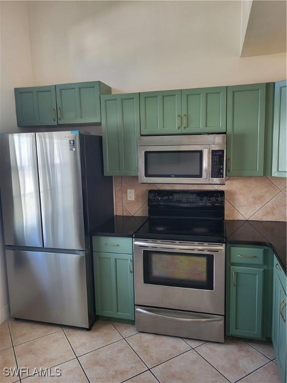 kitchen with light tile patterned floors, backsplash, appliances with stainless steel finishes, and green cabinetry