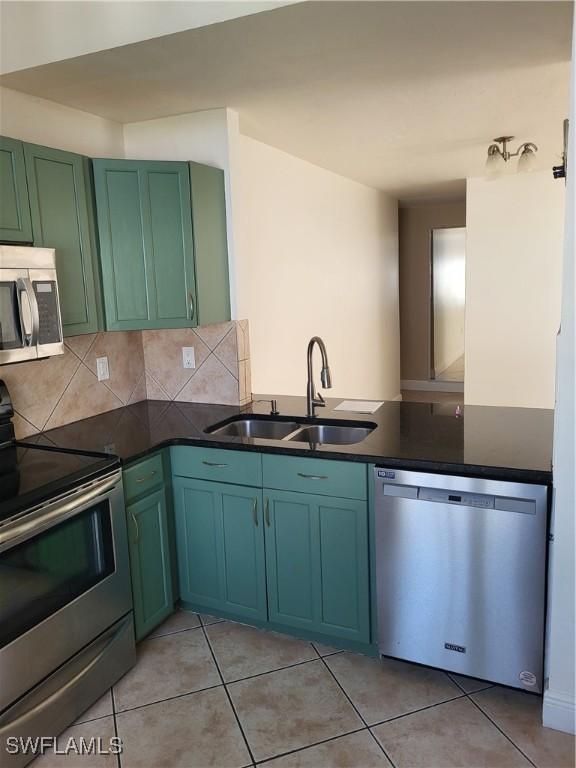 kitchen featuring sink, kitchen peninsula, decorative backsplash, light tile patterned floors, and appliances with stainless steel finishes