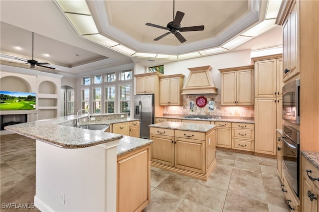 kitchen with appliances with stainless steel finishes, a kitchen island with sink, sink, and a raised ceiling