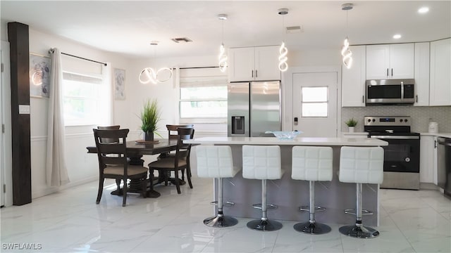 kitchen with decorative backsplash, a kitchen island, white cabinetry, decorative light fixtures, and stainless steel appliances