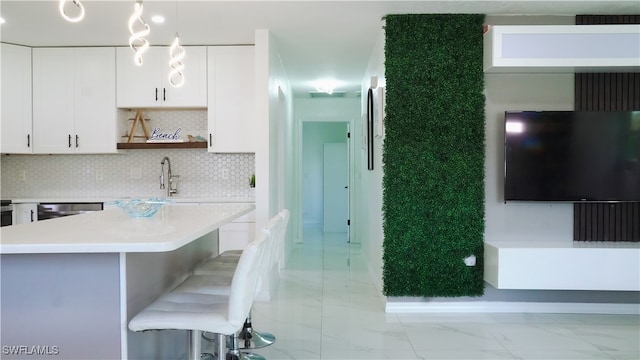 kitchen featuring dishwasher, backsplash, white cabinetry, pendant lighting, and a breakfast bar area