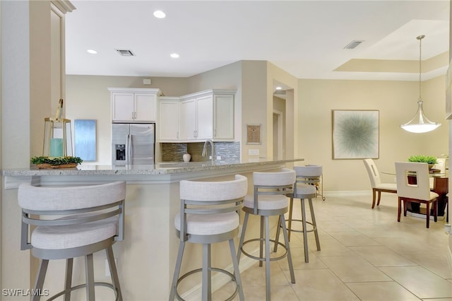 kitchen with kitchen peninsula, tasteful backsplash, white cabinetry, light stone countertops, and stainless steel refrigerator with ice dispenser