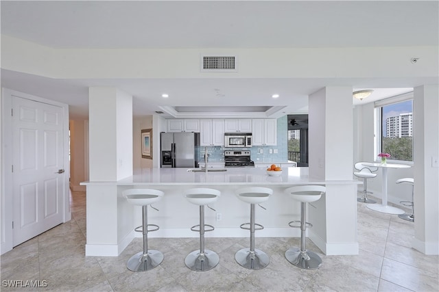 kitchen with tasteful backsplash, appliances with stainless steel finishes, a breakfast bar, and white cabinets