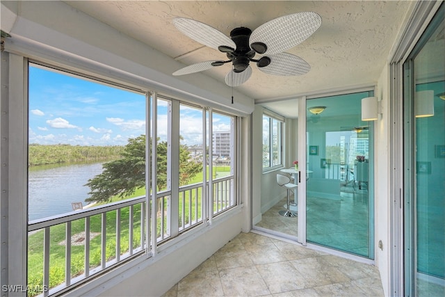 unfurnished sunroom featuring ceiling fan and a water view