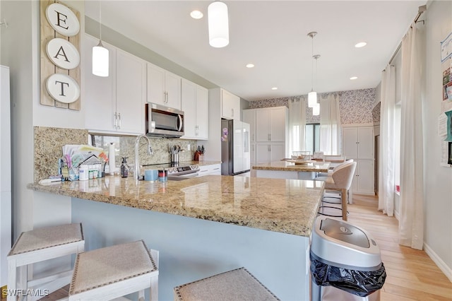 kitchen with appliances with stainless steel finishes, kitchen peninsula, pendant lighting, and white cabinetry