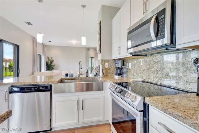 kitchen with kitchen peninsula, white cabinets, hanging light fixtures, appliances with stainless steel finishes, and sink