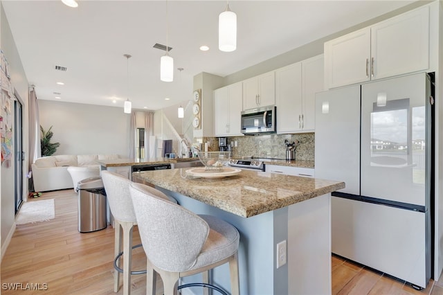 kitchen with light wood-type flooring, a kitchen island, white cabinetry, stainless steel appliances, and decorative light fixtures