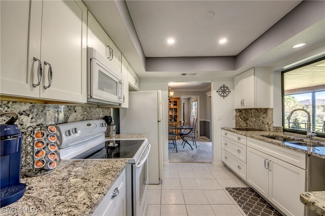 kitchen with sink, white cabinets, light stone counters, and white appliances