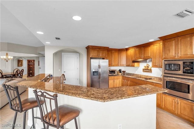 kitchen with light stone countertops, a spacious island, appliances with stainless steel finishes, a notable chandelier, and light tile patterned floors