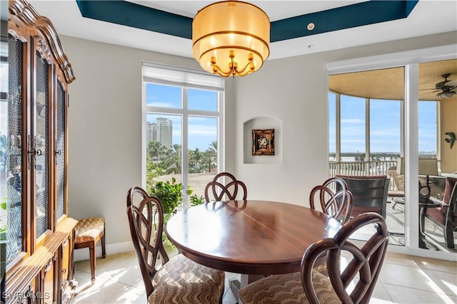 dining space featuring a raised ceiling, light tile patterned floors, and ceiling fan with notable chandelier