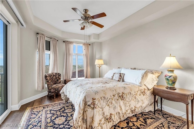 bedroom with ceiling fan, dark wood-type flooring, and a tray ceiling