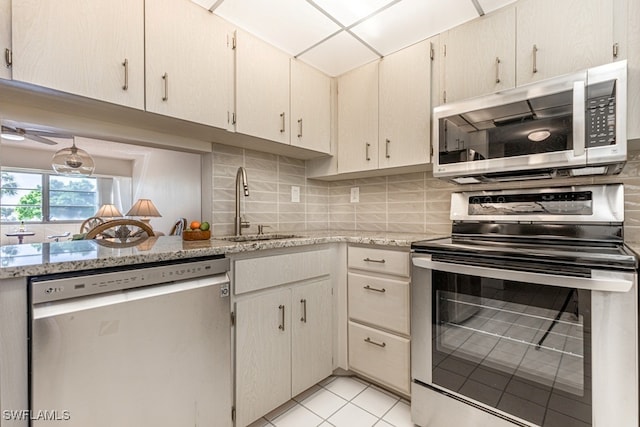 kitchen featuring appliances with stainless steel finishes, sink, backsplash, light stone counters, and light tile patterned floors