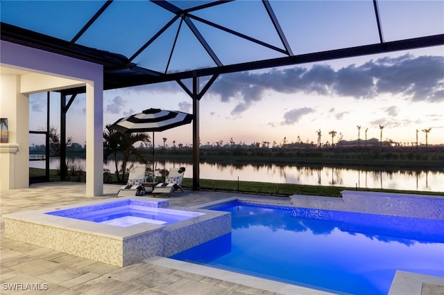 pool at dusk featuring a water view, a patio, glass enclosure, and a pool with connected hot tub