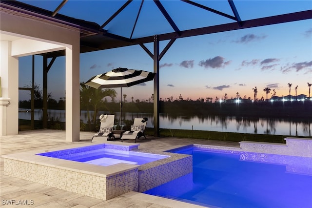 pool at dusk featuring a water view, a patio area, a pool with connected hot tub, and a lanai