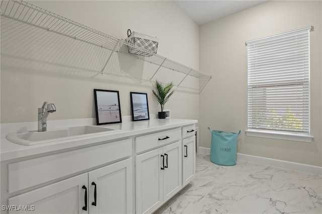 clothes washing area with marble finish floor, a sink, and baseboards