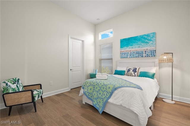 bedroom with a towering ceiling, wood finished floors, and baseboards